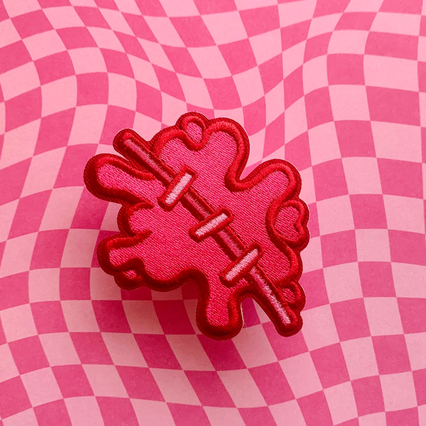 embroidered patch designed like a blood splatter with stitches on a pink checkered background