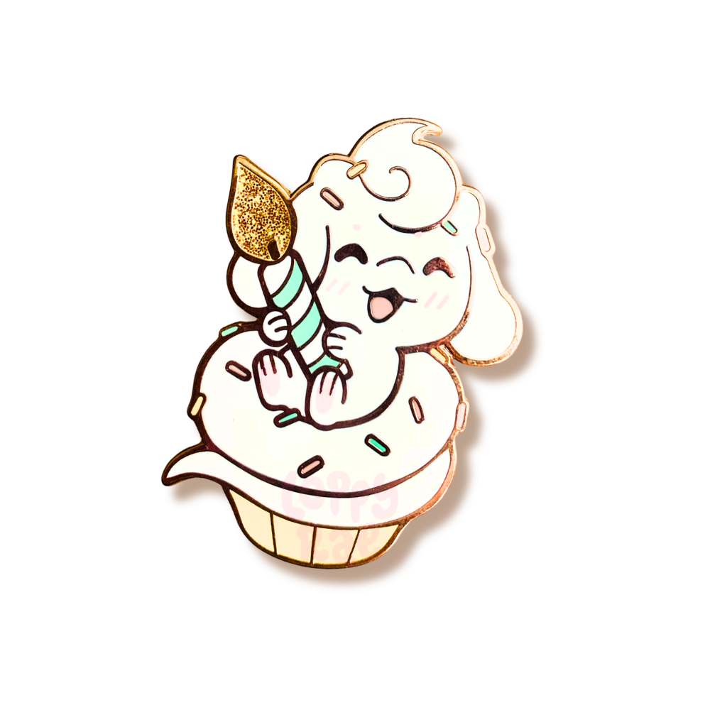 Enamel pin of a cartoon dragon character with a cupcake and candle on a white background