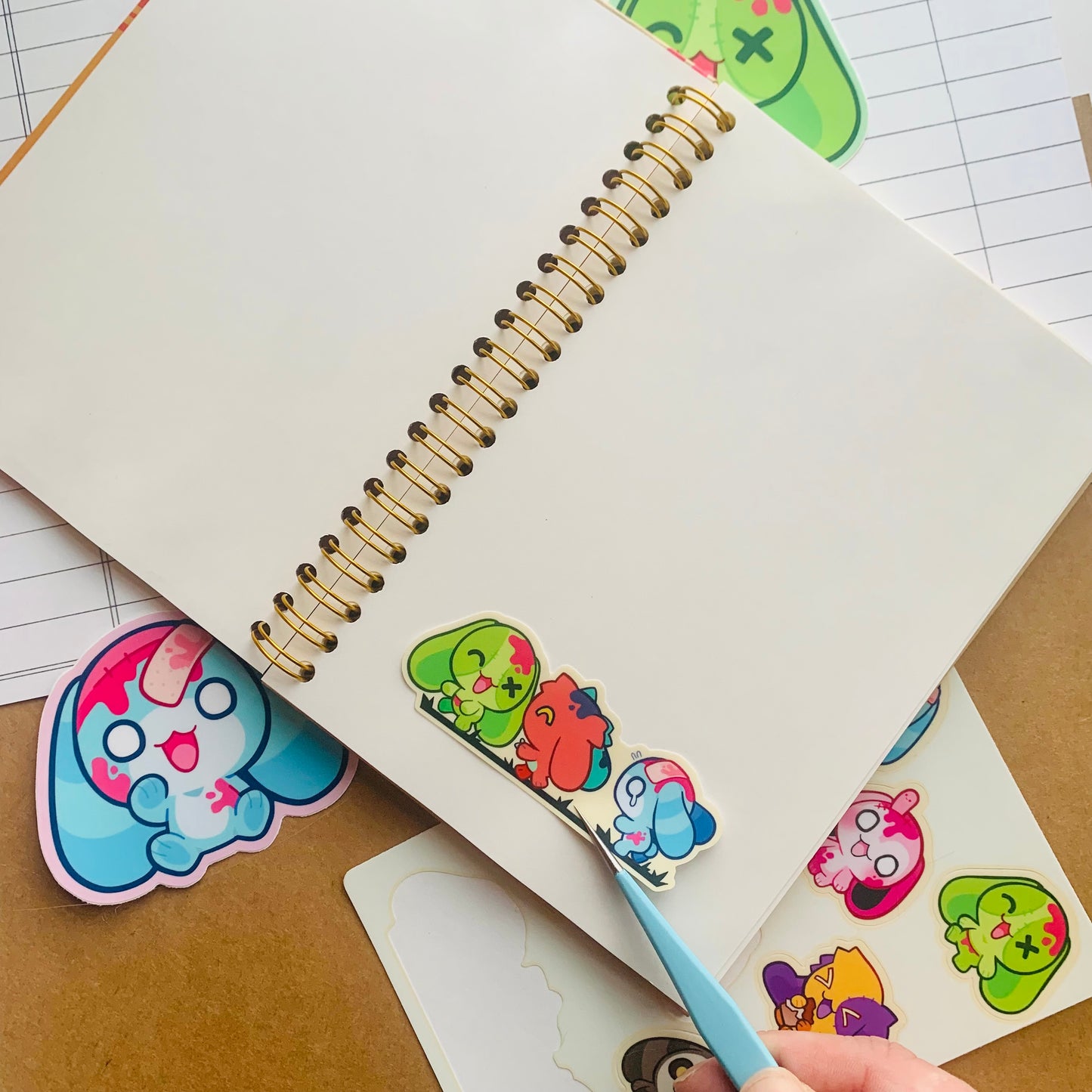 blue tweezers placing cute zombie bunny stickers on the page of an open stickerbook on a paper background