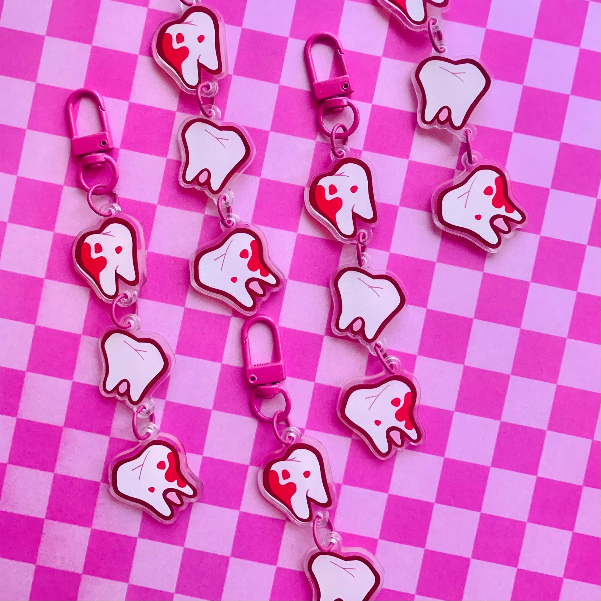 Set of tooth-shaped linking keychain charms on a pink and white checkered background